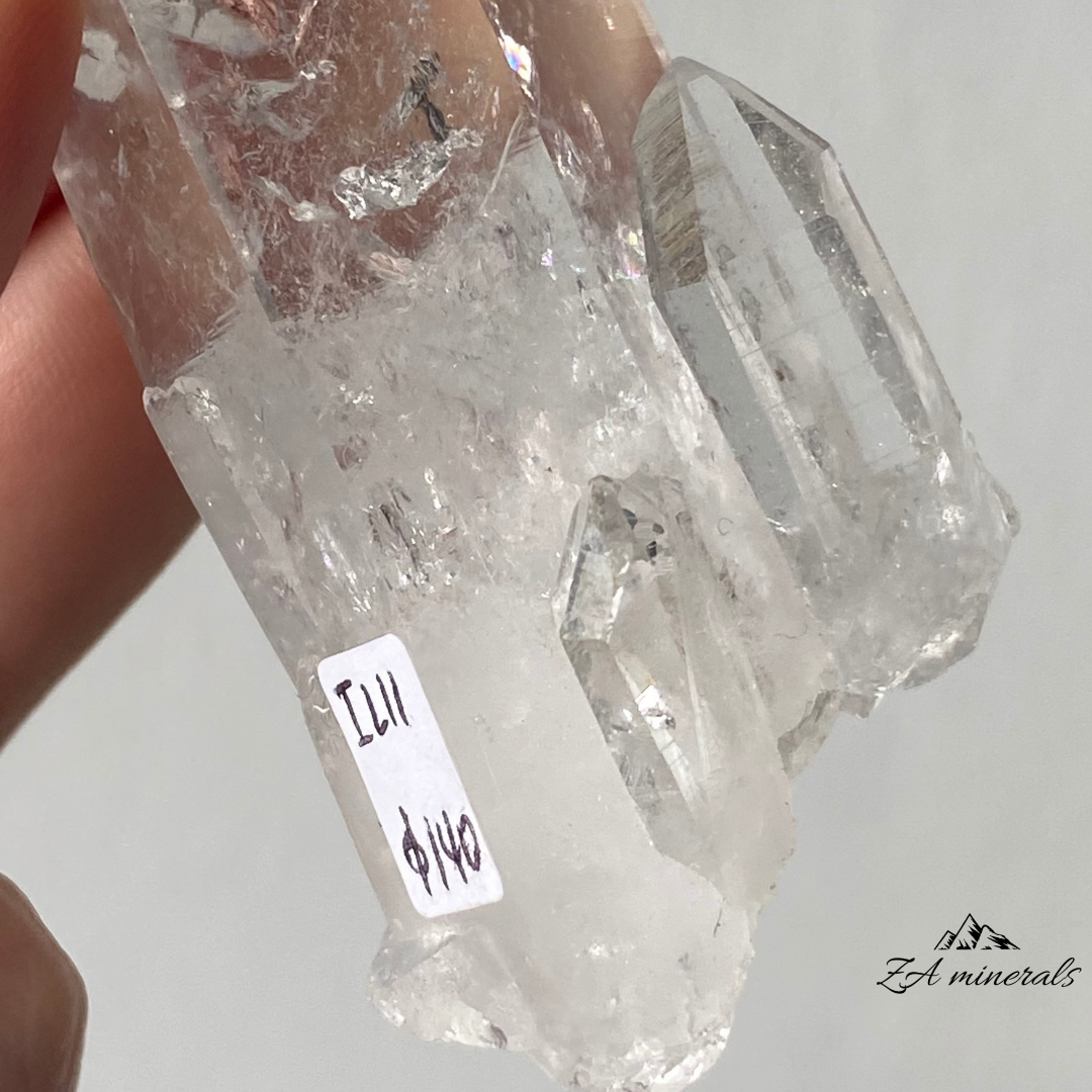 Vitreous, transparent, elongated prismatic Quartz. This quartz is slightly chunky and has secondary quartz development at the base of the crystal body. Internal stress can be seen towards the termination of the crystal. Growth imprint/indentation markings present. Contact damage predominantly to the base of the crystal body. Minor scattered chips to the crystal edges and faces.