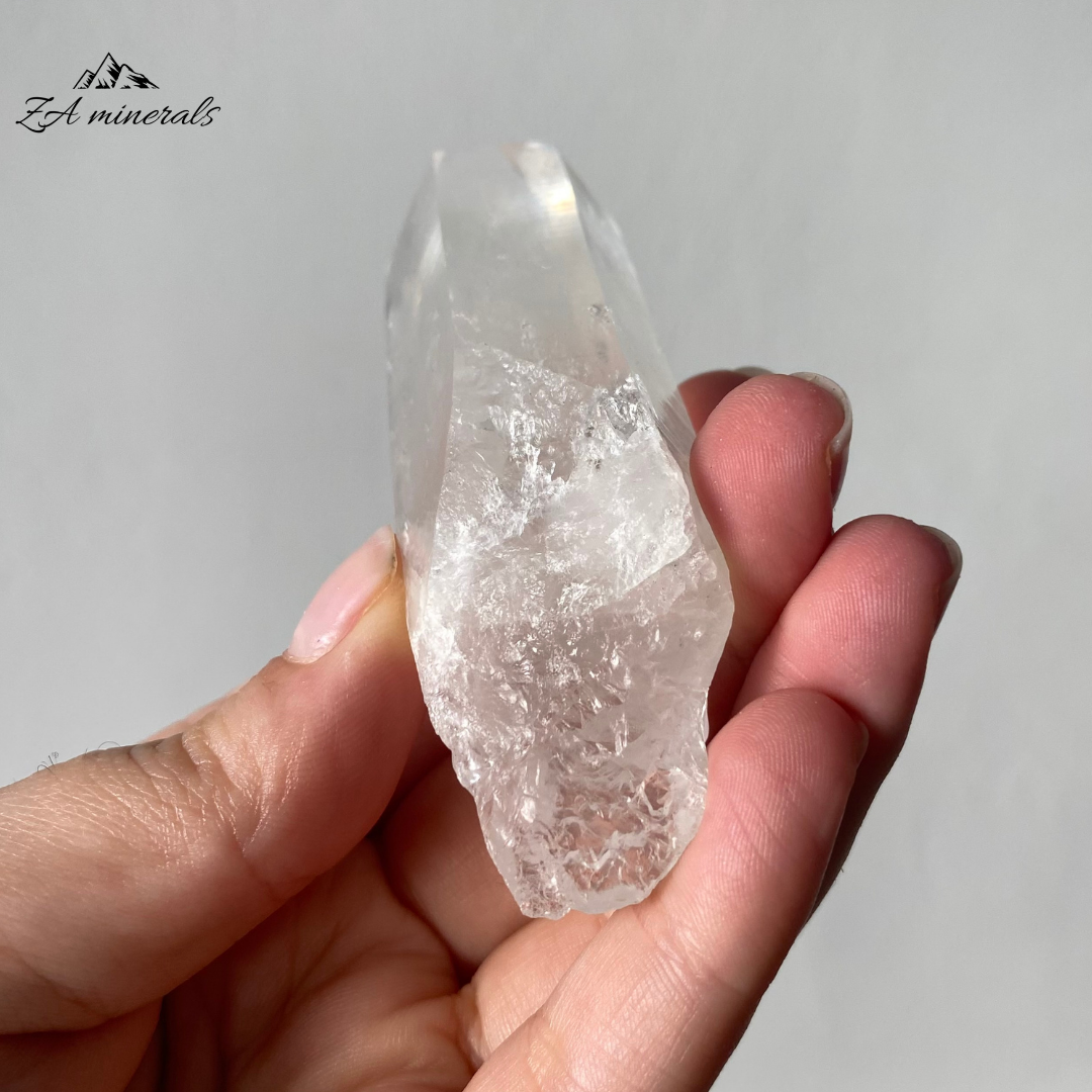 Vitreous, transparent, elongated prismatic Quartz. Milky, very faint Blue 'mist' inclusion in the crystal body. Internal stress can be seen in the crystal body. Growth imprint/indentation markings present. Contact damage predominantly to the base of the crystal body. Minor scattered chips to the crystal edges and faces.