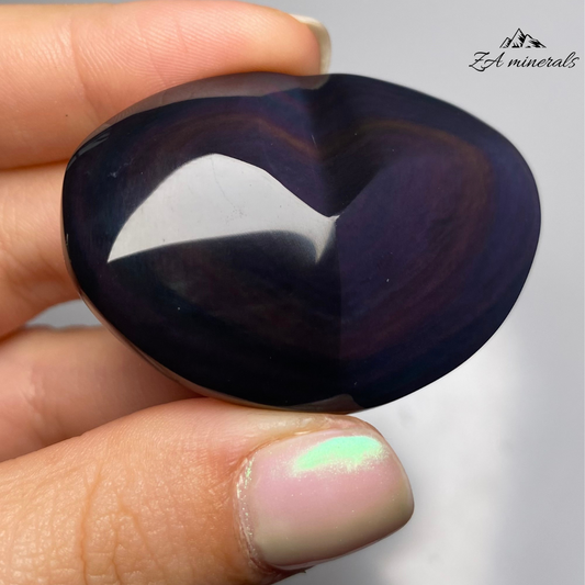 Smooth, opaque, polished heart of Obsidian. Obsidian has a black colour to it. Surface of the Obsidian heart exhibits a display of colours -vibrant blue and purple tones. Little to no scratches or imperfections on the surface of the carving.