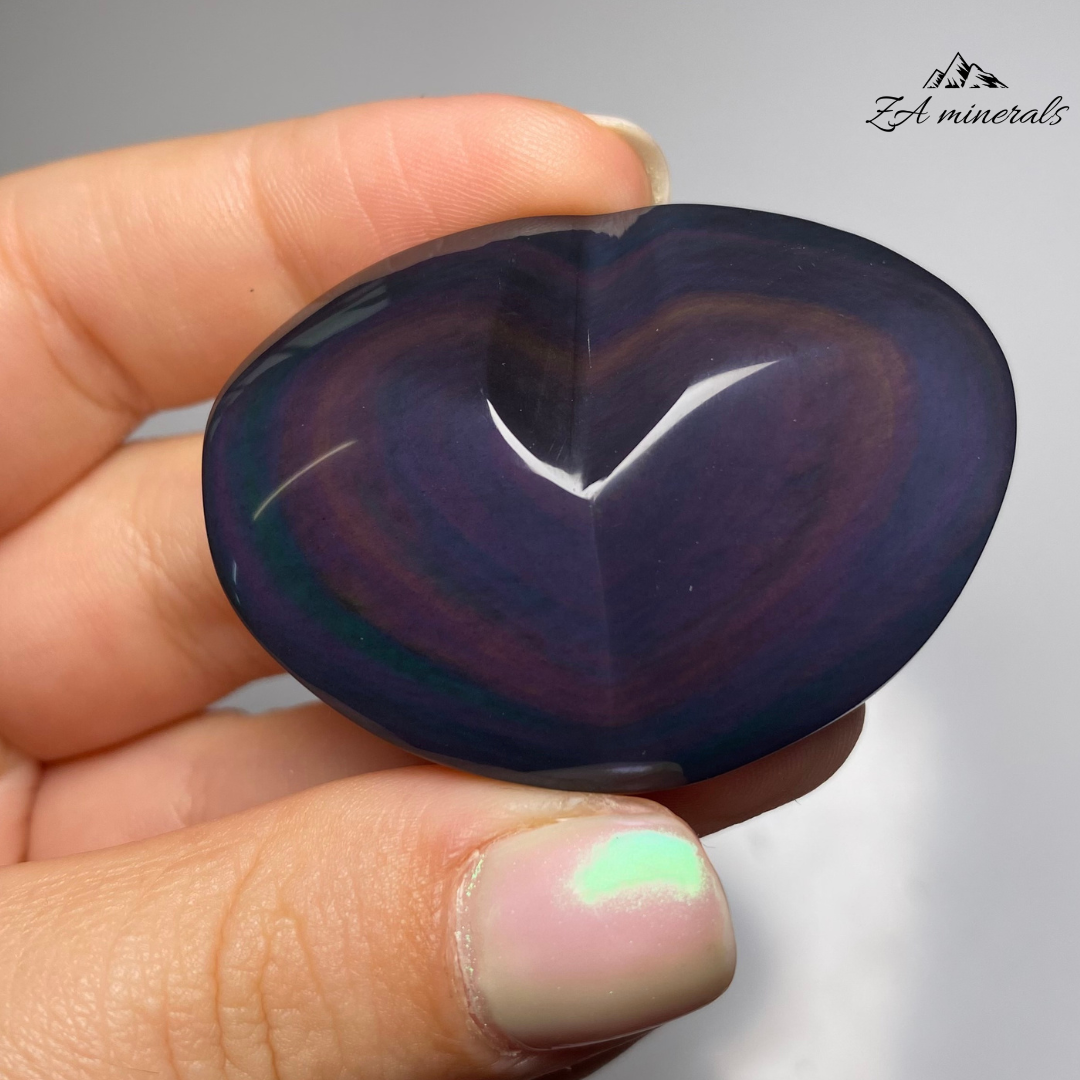 Smooth, opaque, polished heart of Obsidian. Obsidian has a black colour to it. Surface of the Obsidian heart exhibits a display of colours -vibrant blue and purple tones. Little to no scratches or imperfections on the surface of the carving.