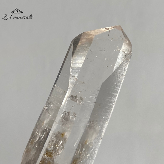 Vitreous, transparent, elongated prismatic Quartz. This quartz is slightly chunky. The termination has a large Isis Face.  Contact damage predominantly to the base of the crystal body. Minor scattered chips to the crystal edges and faces.