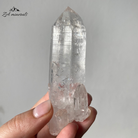 Vitreous, transparent, elongated prismatic Quartz. This quartz is slightly chunky and has secondary quartz development at the base of the crystal body.  Internal stress can be seen towards the termination of the crystal. Growth imprint/indentation markings present. Contact damage predominantly to the base of the crystal body. Minor scattered chips to the crystal edges and faces.