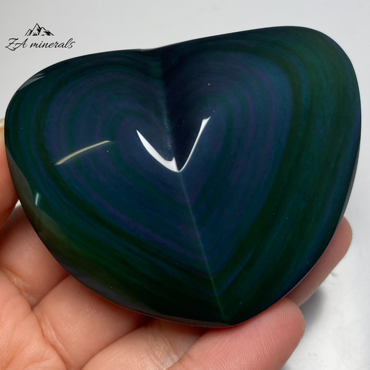 Smooth, opaque, polished heart of Obsidian. Obsidian has a black colour to it. Surface of the Obsidian heart exhibits a vibrant display of colours -blues and greens Little to no scratches or imperfections on the surface of the carving.