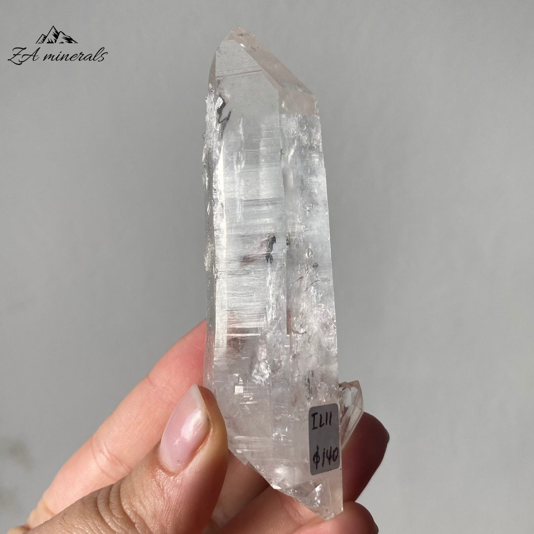Vitreous, transparent, elongated prismatic Quartz. This quartz is slightly chunky and has secondary quartz development at the base of the crystal body.  Internal stress can be seen towards the termination of the crystal. Growth imprint/indentation markings present. Contact damage predominantly to the base of the crystal body. Minor scattered chips to the crystal edges and faces.