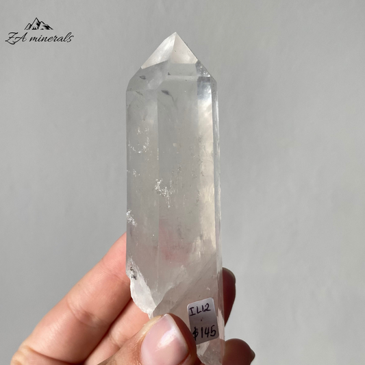 Vitreous, transparent, elongated prismatic Quartz. Milky, very faint Blue 'mist' inclusion in the crystal body. Internal stress can be seen in the crystal body. Growth imprint/indentation markings present. Contact damage predominantly to the base of the crystal body. Minor scattered chips to the crystal edges and faces.
