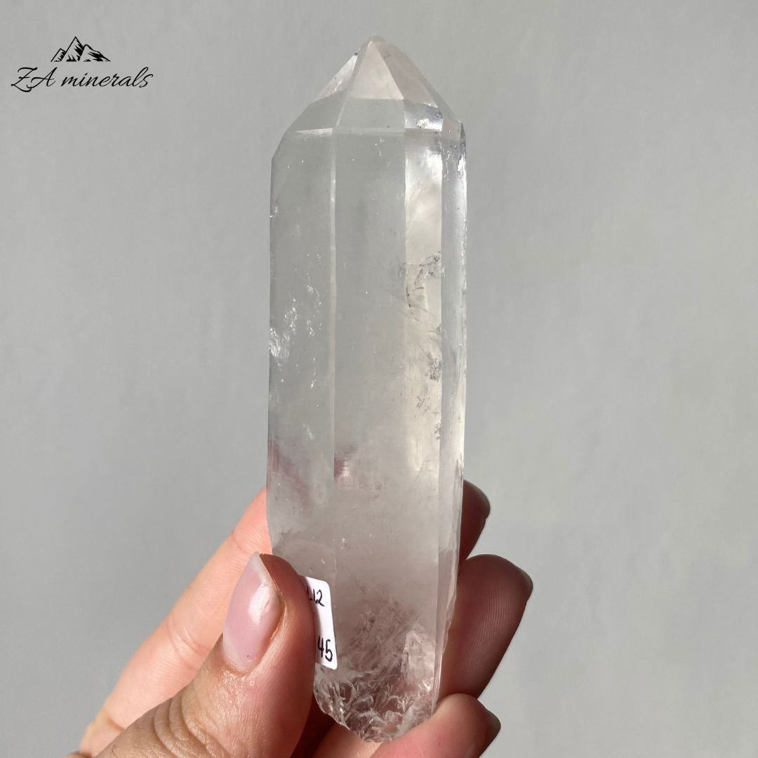 Vitreous, transparent, elongated prismatic Quartz. Milky, very faint Blue 'mist' inclusion in the crystal body. Internal stress can be seen in the crystal body. Growth imprint/indentation markings present. Contact damage predominantly to the base of the crystal body. Minor scattered chips to the crystal edges and faces.