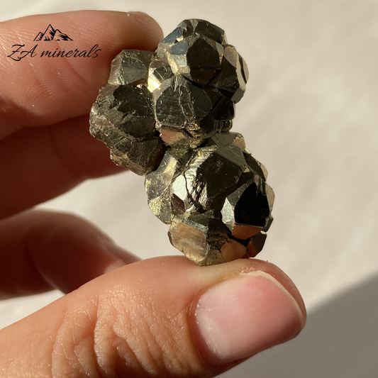 Pyrite crystal held between fingers with 'ZA minerals' branding.