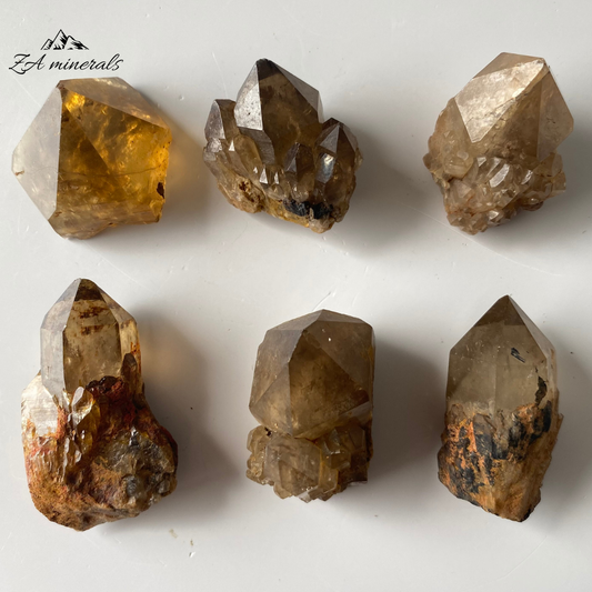 Small yet powerful, these Kundalini Citrine points are ideal for gridding. Their warm energy is perfect for manifesting wealth and prosperity.  Vitreous, prismatic, translucent to sub-opaque Kundalini Citrine singles. Rich Honey Brown to Smoky Brown hue of the citrine singles. Some of the Singles have artichoke development present. Matte, opaque, grey-black Goethite can be seen on one of the singles. Scattered chips to the crystal edges and terminations.