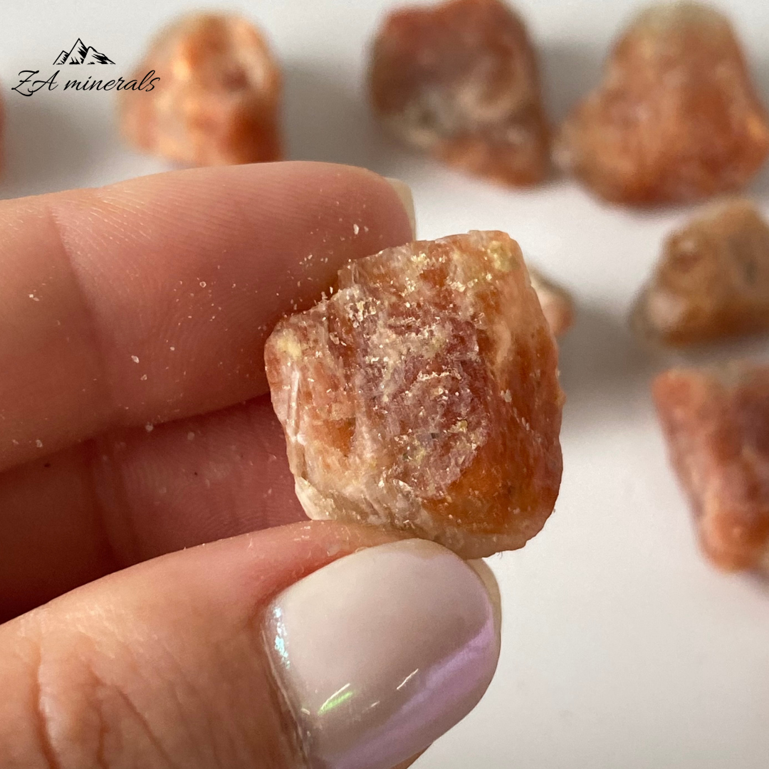 A variety of feldspar (microcline or oligoclase) that has schiller, commonly with an orange/brown background color, due to exsolved oriented small hematite crystals that give it a flash and sparkle. These rough chunks of Sunstone have a matte luster. Subtle orange hue to the Sunstone chunks. When the sunstone is held at particular angles the vibrant Orange Schiller of the Sunstone can be seen. These are rough chunks and do not have a crystallized shape.