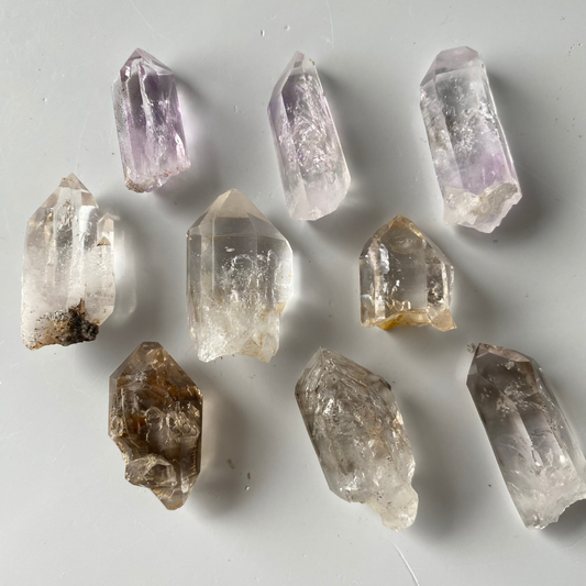 Vitreous, transparent to translucent, prismatic Quartz crystals. Subtle lavender-Amethyst zoning can be seen in three (3) of the Quartz crystals. One (1) of the Quartz crystals has a moving enhydro water bubble. Three (3) of the Quartz are clear and colourless. Three (3) of the Quartz have lovely saturated Smoky zoning present.  Chip to the termination of the one amethyst Quartz. Damage to the base of the crystals. Minor scattered chips to the crystal edges.